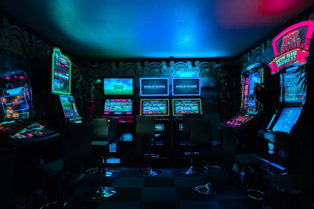 A dedicated home game room with two full-size arcade cabinets mounted on matching powder-coated steel stands, warm overhead lighting, and neatly routed cables disappearing into lockable bases